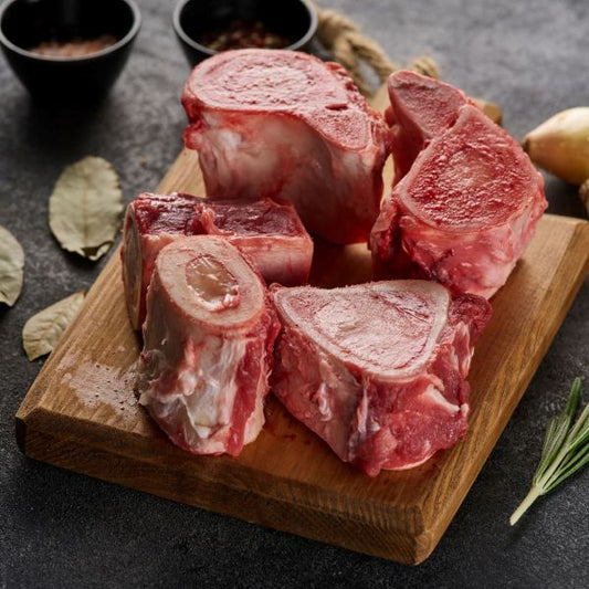 Raw beef bones on a wooden cutting board with spices and herbs on a dark surface