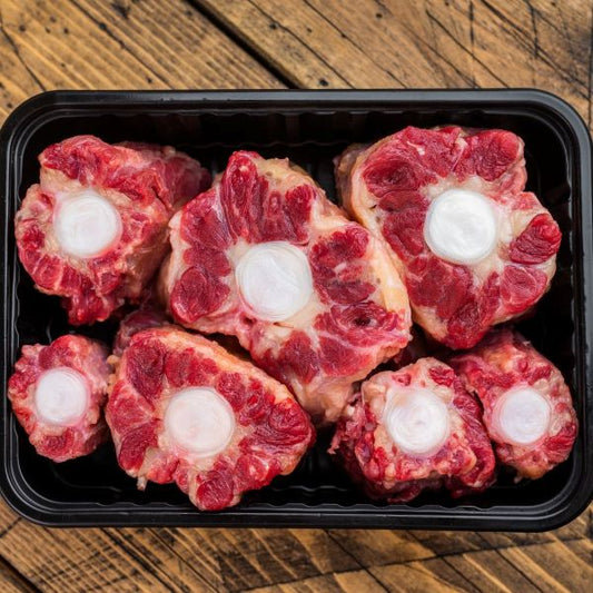 Raw beef oxtail bones with marrow in a black plastic container on a wooden surface
