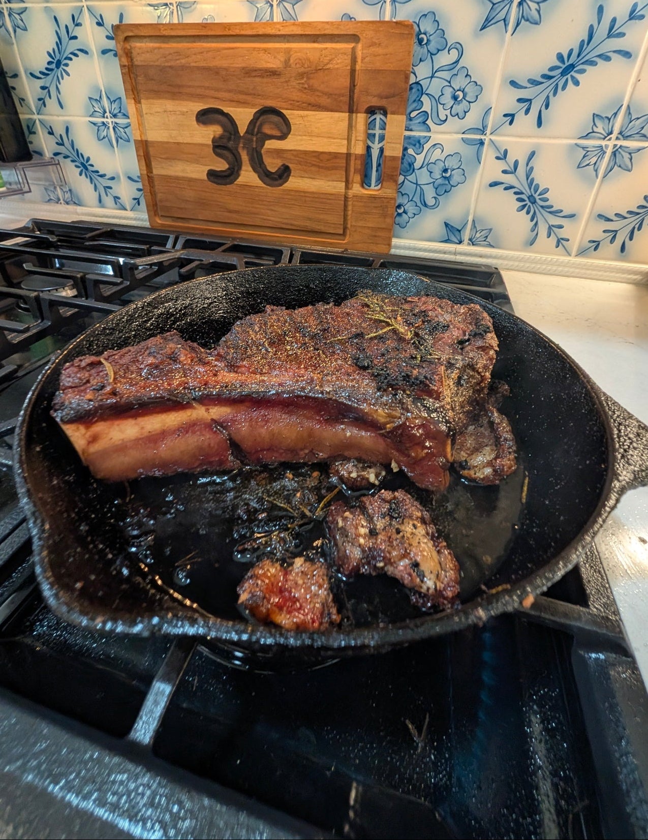 Wagyu beef cooking in a cast iron skillet on a stove with a wooden cutting board in the background.